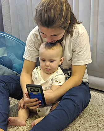 Robyn Coggins sitting with her infant son Henry looking at her phone
